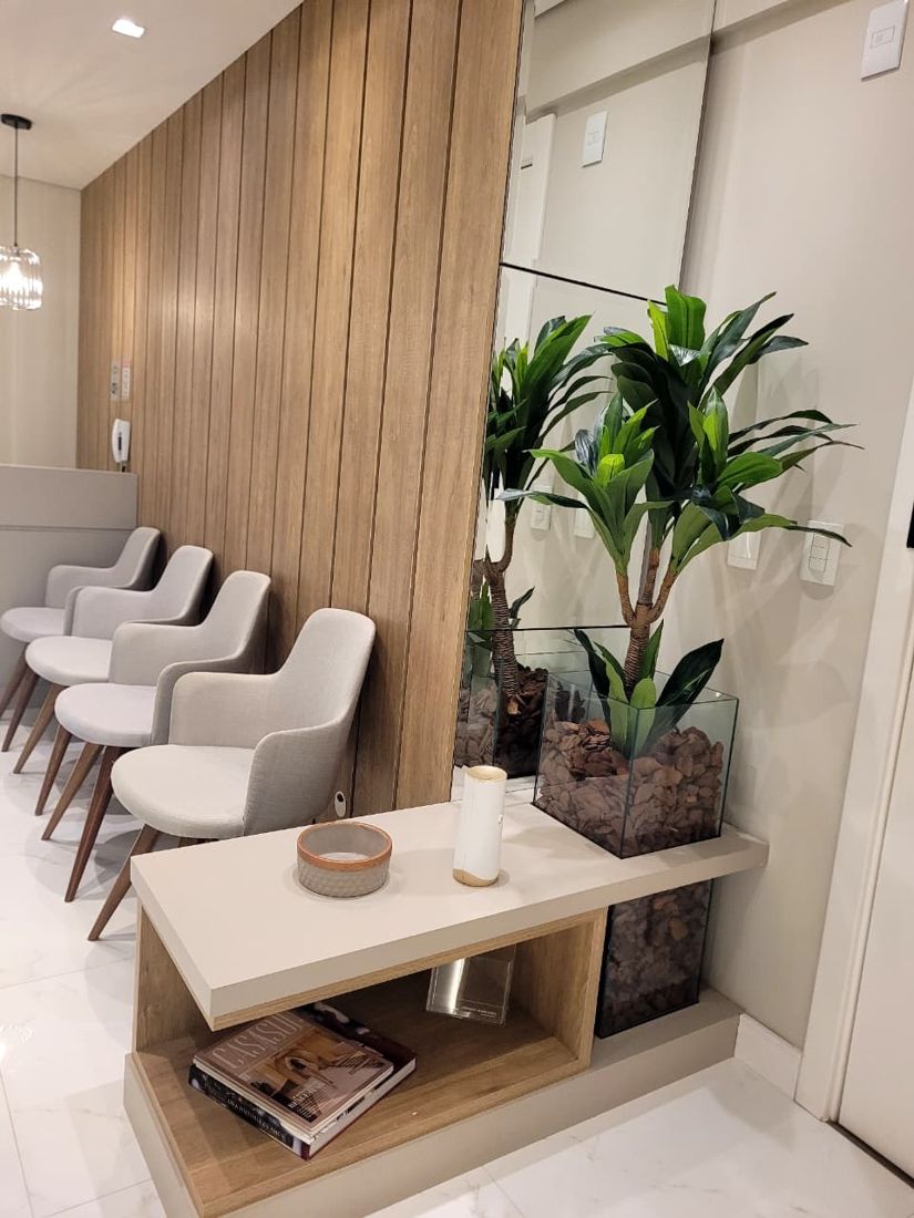 Recepção da VIVENS com poltronas claras, painel de madeira e planta